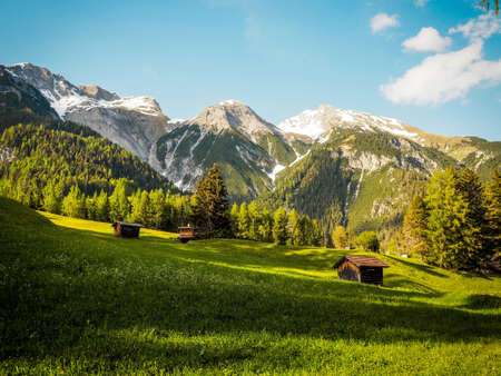 A scenic view of the alps in summer with lush green grass surrounding an old shack