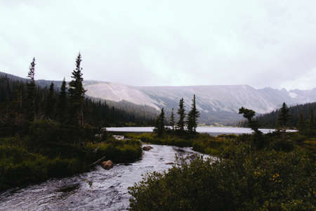 A beautiful natural scenery with a river connecting to a lake with pine trees and hills in the backgroundの写真素材