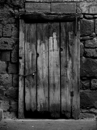A black and white shot of an old wooden door of a stone houseの写真素材