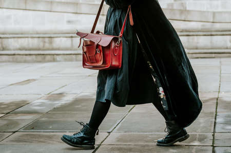 A person in a black coat carrying satchel bag while walking on the streetの写真素材