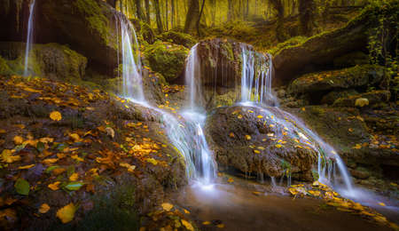 A long exposure shot of a small waterfall on the rocks with fallen leaves in autumn