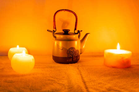 A closeup shot of burning candles teapot and cups on dark backgroundの写真素材