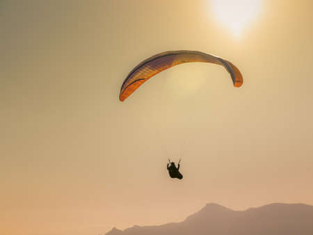 A person paragliding above the mountains under the sunlight during the sunset