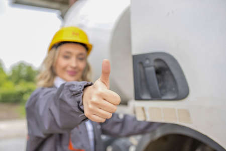 A closeup of a happy female construction worker doing the thumbs-up gesture under the sunlightの写真素材