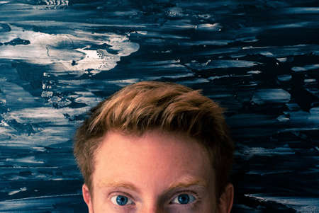 The eyes of a blond man in front of the blue abstract wallの写真素材