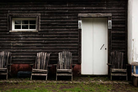 A wooden house with a white door and two wooden chairs in frontの写真素材