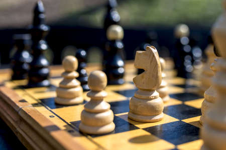 A closeup shot of the chessboard with chess pieces on blurred background under a sunlight