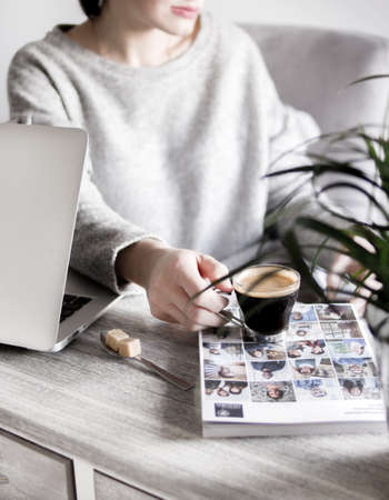 A female in a white sweater drinking coffee next to a laptop and a photography magazineの写真素材