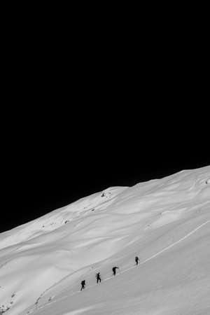 Hikers walking up a steep snowy hill at night with pitch black sky in the background