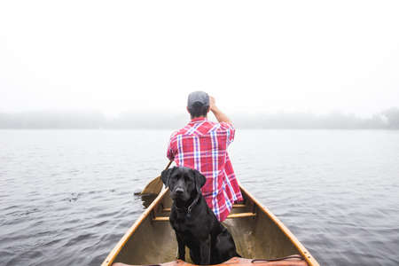 A beautiful shot of a black dog and a male sailing on a small boat on body of waterの写真素材