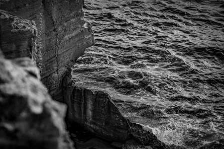 A beautiful shot of sea waves near the cliff in black and white
