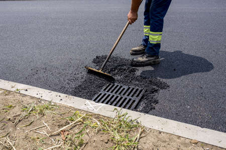 A person cleaning the road after laying down asphalt under the sunlightの写真素材