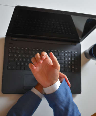 A high angle view of a businessman fixing his cufflinks with a laptop on the background