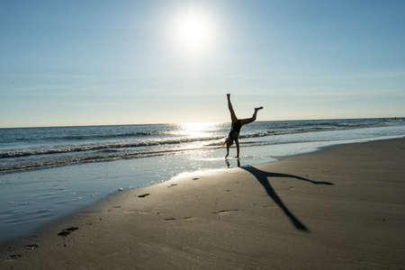 A fit male doing a handstand at the sunny sandy beachの写真素材