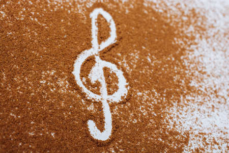 A high angle shot of brown species sprinkled on a white background and  musical clef on the centerの写真素材