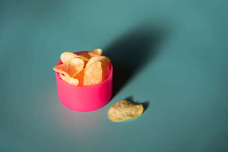 A closeup shot of plain potato chips in a plastic pink bowl and crumbs on a blue backgroundの写真素材