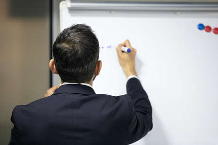 A businessman on a meeting writing on a whiteboard with a marker
