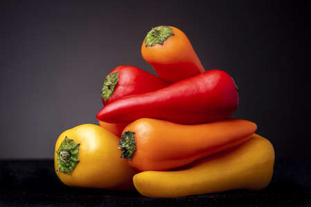Yellow, red and orange colourful peppers stacked on top of each other. Studio low key food still life.の写真素材