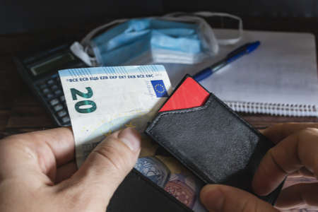 A high angle shot of a person holding a wallet and a banknote with different items on the background