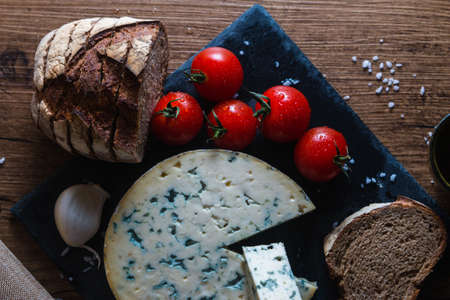 A round blue cheese surrounded by bread, tomatoes and garlicの写真素材