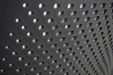 A closeup shot of a black metallic surface with symmetrical holes on it