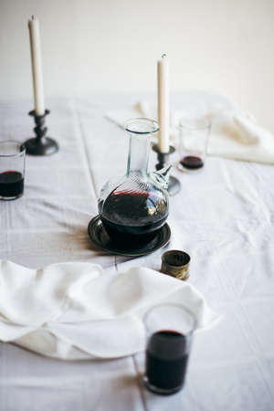 A messy table setting after dinner with half drunk glasses of red wine, a carafe and white damask...