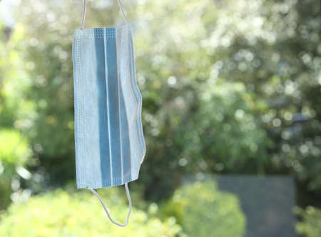 A selective focus shot of a blue medical mask with trees on the background