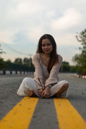 A young Asian female with long hair wearing a white dress with a jacket sitting in the middle of the...
