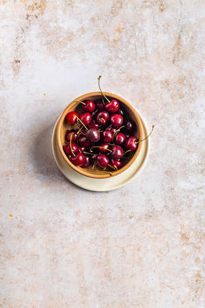 A vertical image of red ripe cherries in a bowl on a concrete surface with space for your textの写真素材