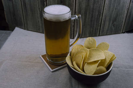 A closeup shot of crisps and a glass of beer on the table with a wooden backgroundの写真素材