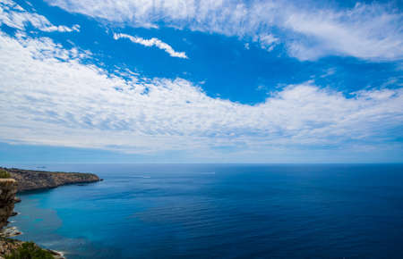 The land next to the water under the blue sky full of cloudsの写真素材