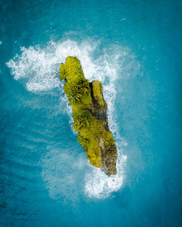 An aerial shot of a beautiful green little island in the middle of the ocean