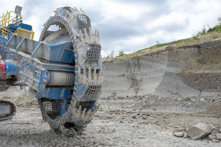 A closeup of a bucket wheel excavator at a quarry site under a cloudy sky