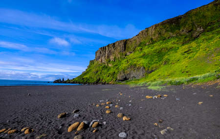 A seashore near a grassy hill and a cliff with a blue sky in the backgroundの写真素材