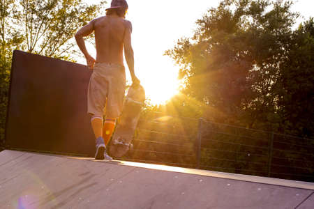 A young male skateboarding in a park surrounded by trees under the sunlightの写真素材