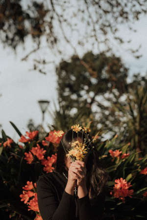 A female holding a bouquet of wildflowers in front of her face in a garden with a natural background...