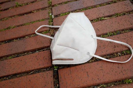 A white protective  dirty face mask thrown on the ground