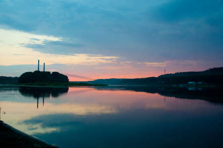 A wide shot of a sea near trees and mountains at sunset at Kemerovo