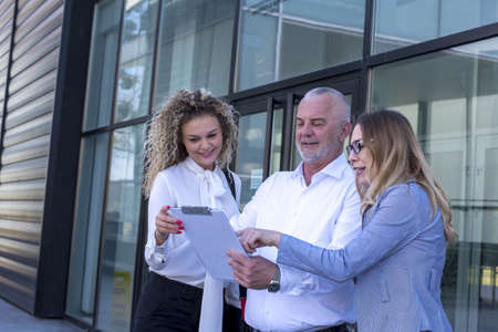 A group of colleagues looking at note board and discussing a project in front of the office building