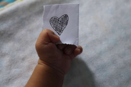 A closeup shot of a child hand holding a paper with a heart drawing