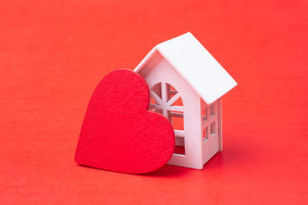 A closeup of a small house figure with a heart shape isolated on a red backgroundの写真素材