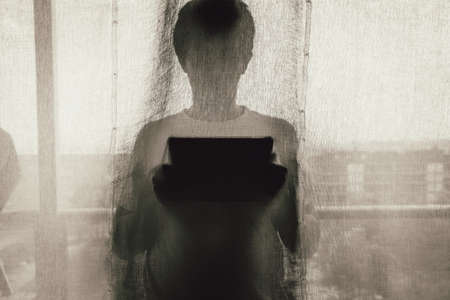A silhouette of a person holding a tablet computer covered with window blinders
