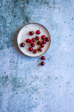 A vertical image of red ripe cherries on a saucer on a concrete surface with space for your textの写真素材