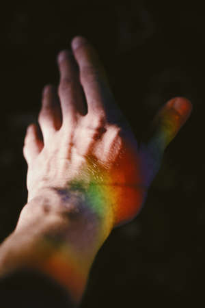 A hand of a male with a rainbow texture on the side with a pitch black backgroundの写真素材