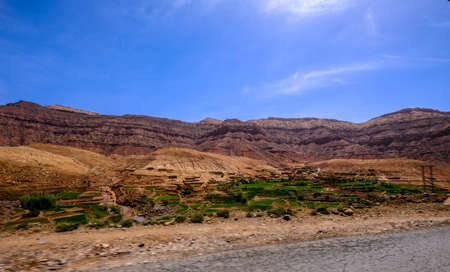 A road near the grassy fields with sandy mountains in the distance and a blue sky in the backgroundの写真素材