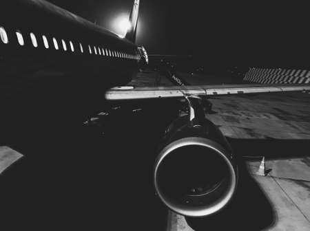 A closeup black and white shot of an airplane engine on a runway with the shining moon in the backgroundの写真素材