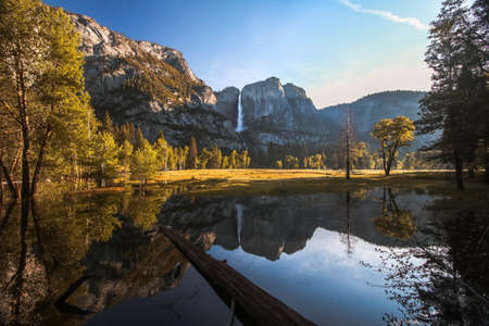 A beautiful wide shot of a lake surrounded by trees and mountains under a clear sunny skyの写真素材