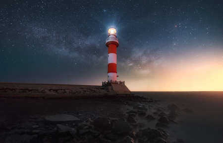 The starry night sky over the burning lighthouse on the coast of the seaの写真素材