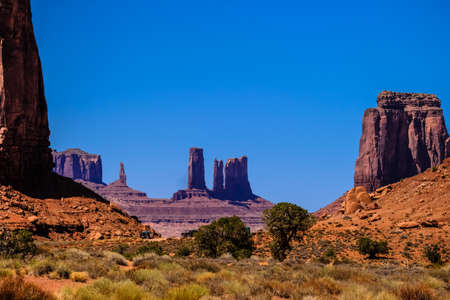 A desert with dried bushes and trees with big rocks on hills in the distance on a sunny day