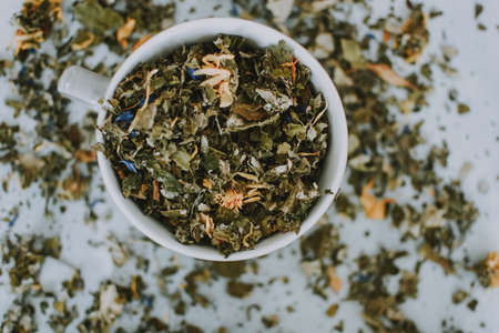 A closeup shot of a white bowl full of dried leaves on a white blurred backgroundの写真素材